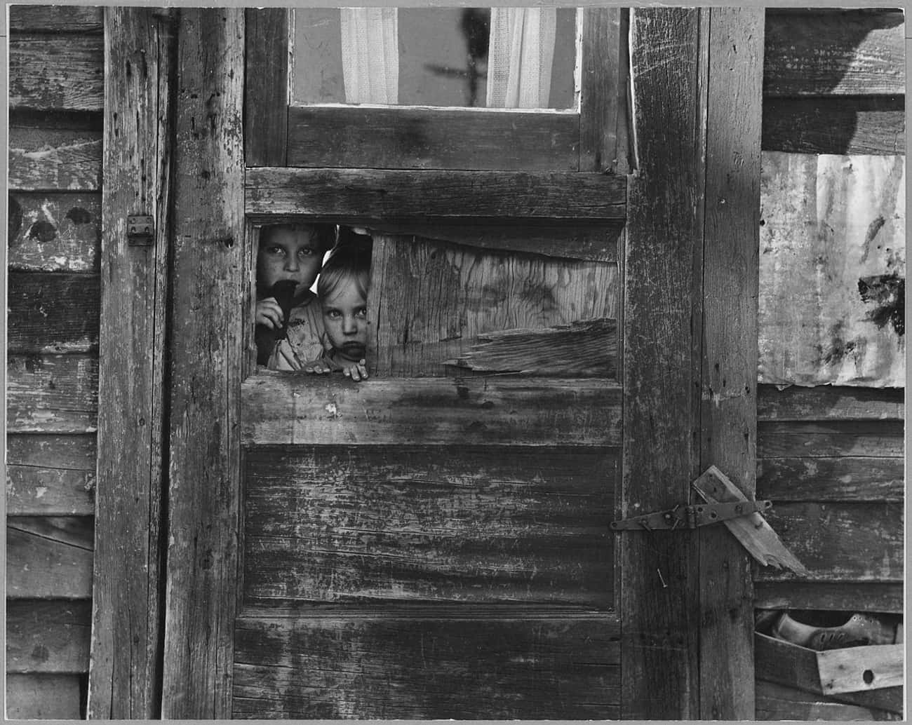 Two Children In A Camp Peek Through A Door In Kern County, CA, 1940